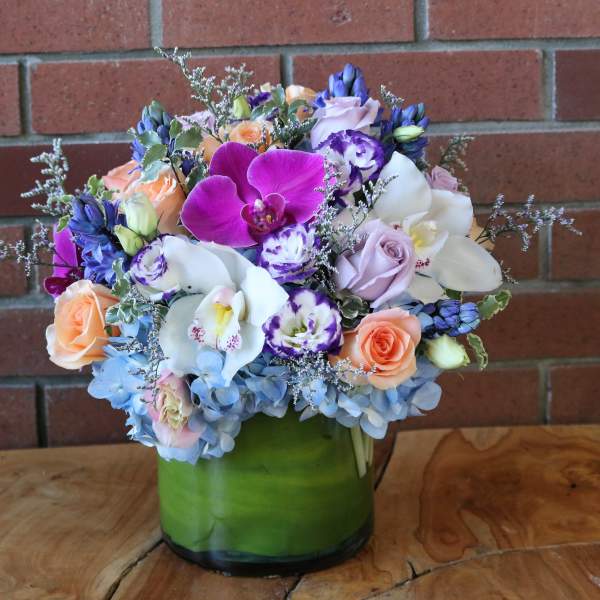 Mixed bouquet of orchids, roses, and hydrangeas in a green glass vase