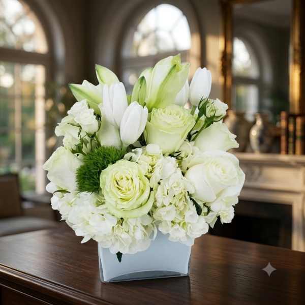 White floral arrangement in a square vase with lilies and roses