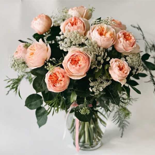 Peach garden roses and white filler flowers arranged in a clear glass vase