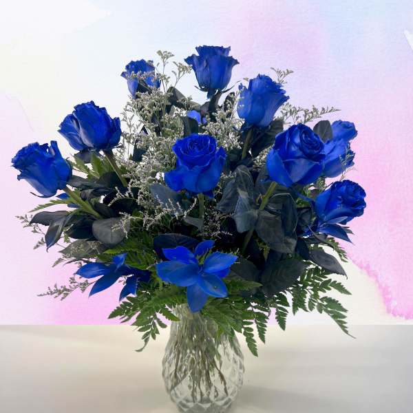 Blue roses arranged in a clear glass vase with greenery