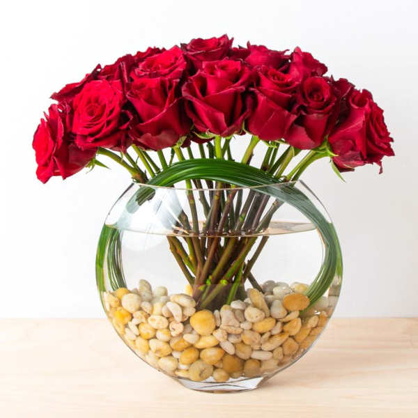 Red roses arranged in a round glass vase with pebbles