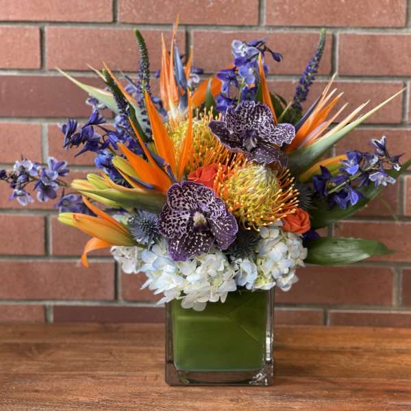 Tropical bouquet in a square glass vase with orange and purple flowers