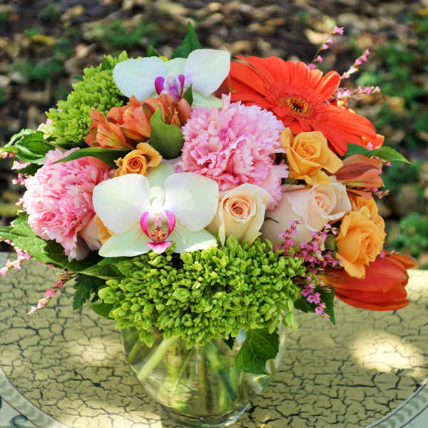 Mixed bouquet of pink carnations, roses, orchids, and orange blooms in a clear glass vase