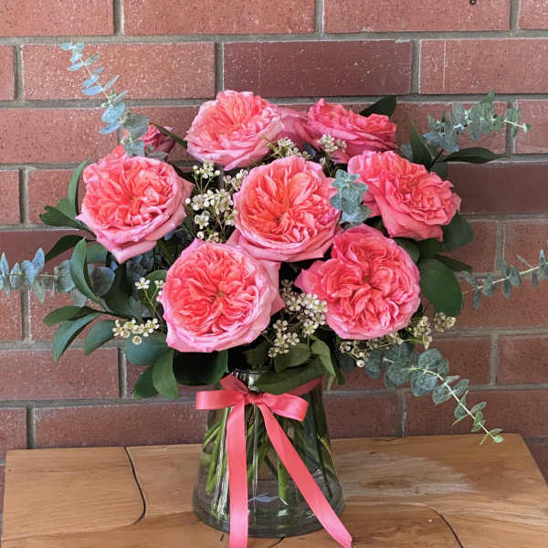 Pink roses in a glass vase with eucalyptus and a pink ribbon