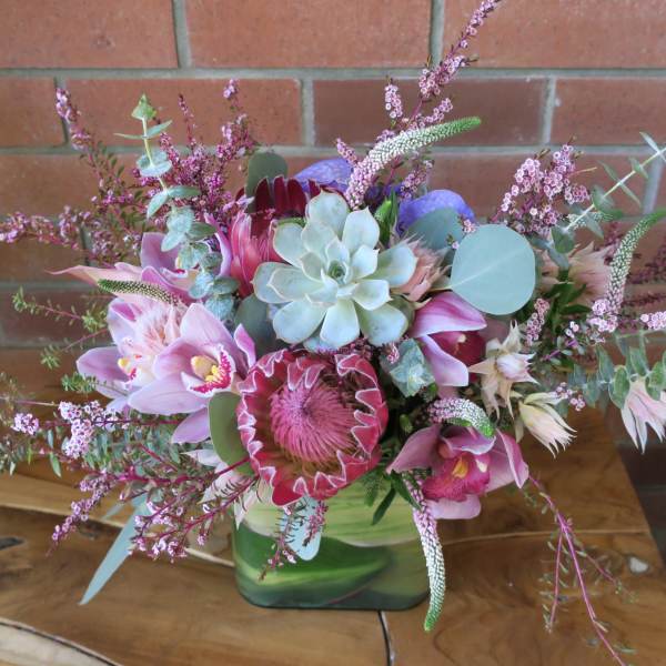 Pink and purple floral arrangement in a green vase with succulents
