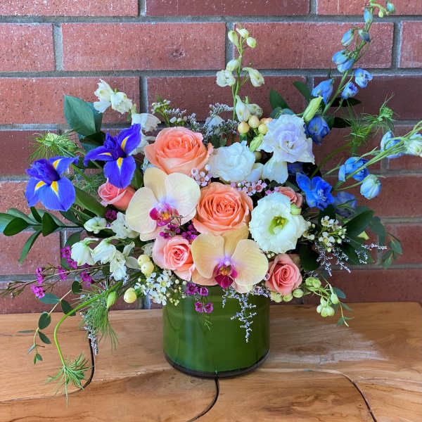 Mixed bouquet in a green glass vase with peach roses and blue irises