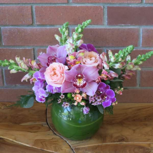 Pink and purple flowers arranged in a green glass vase