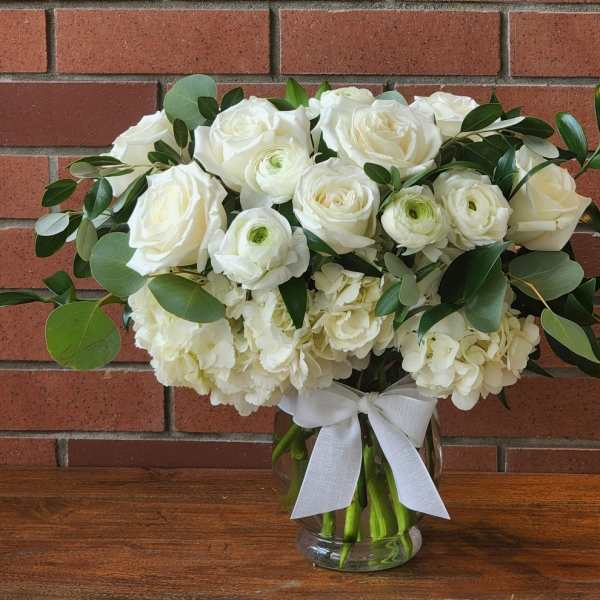 White roses and ranunculus in a glass vase with a white ribbon