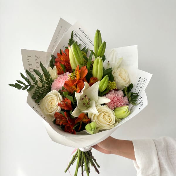 Hand-tied bouquet of white roses, lilies, and orange flowers in white paper