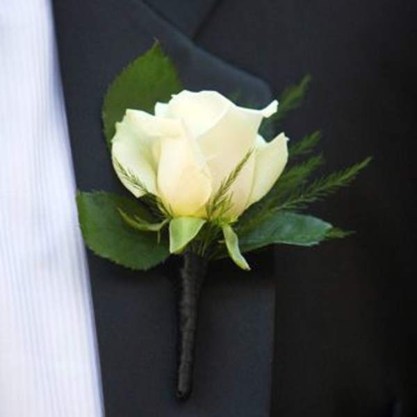 White rose boutonniere with greenery pinned to a black suit jacket
