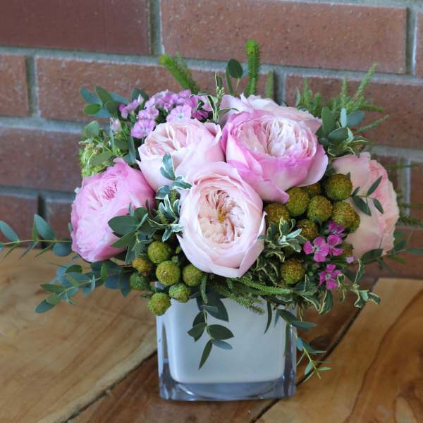 Pink roses arranged in a square glass vase with greenery