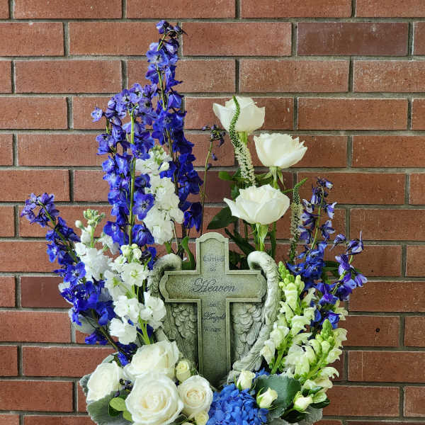 White roses and blue flowers arranged around a memorial cross in a basket