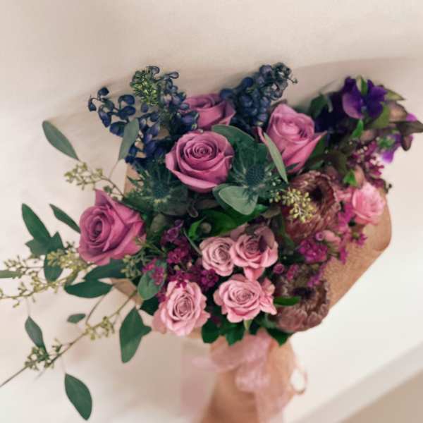Bouquet of pink and purple roses with greenery and a pink ribbon