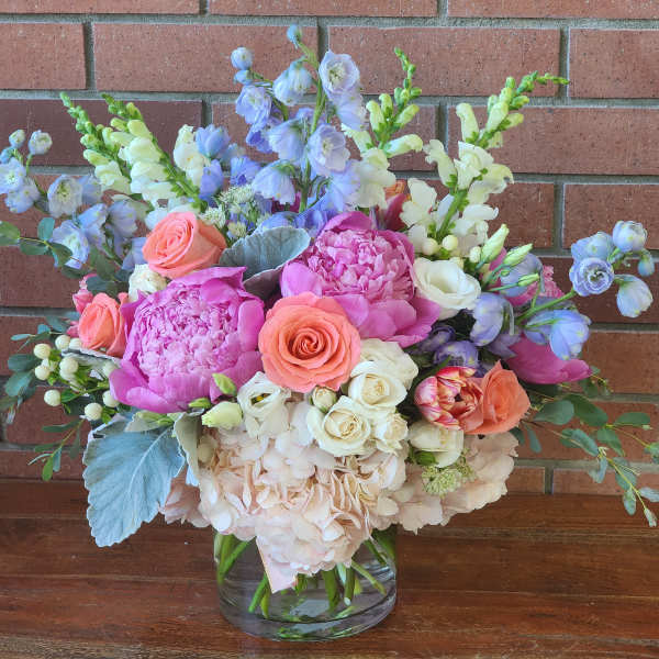 Mixed bouquet of pink, peach, white, and blue flowers in a glass vase