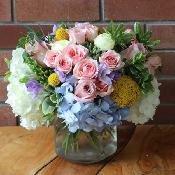 Bouquet of pink roses, hydrangeas, and yellow accents in a glass vase