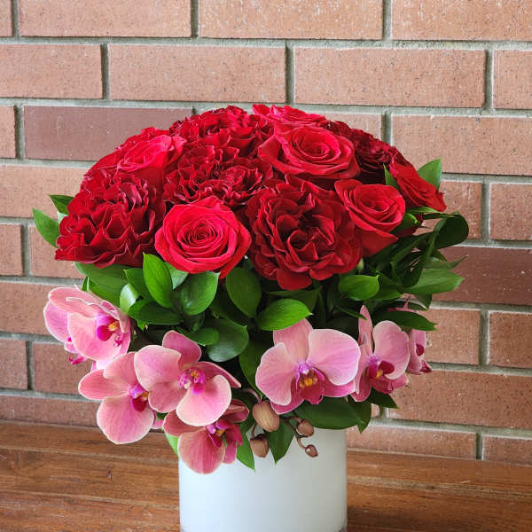 Red roses and pink orchids arranged in a white vase