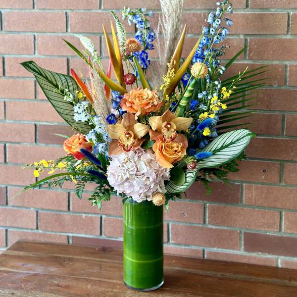 Tropical bouquet in a tall green vase with orange and blue flowers