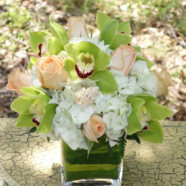 Bouquet of pale roses, white hydrangeas, and green orchids in a square glass vase