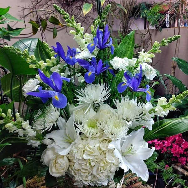 Tall arrangement of blue irises and white lilies, hydrangeas, and mums in a woven basket