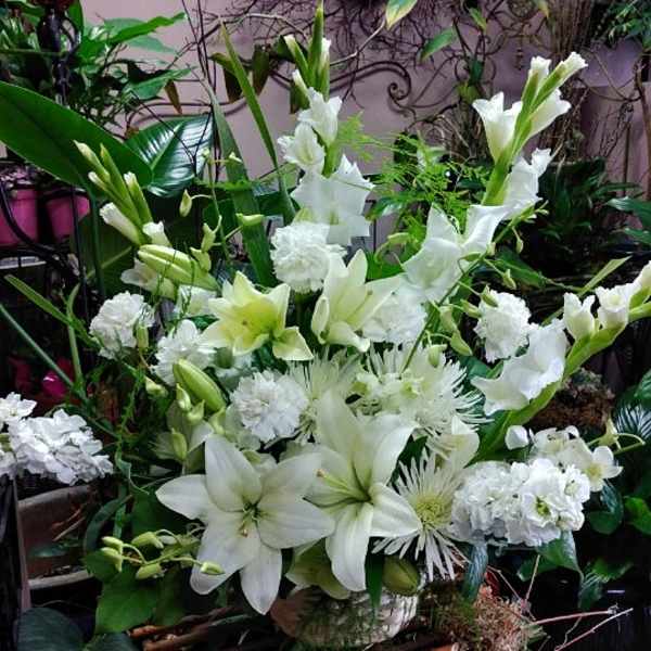 Tall all-white floral arrangement with lilies, carnations, and other blooms in a ceramic container