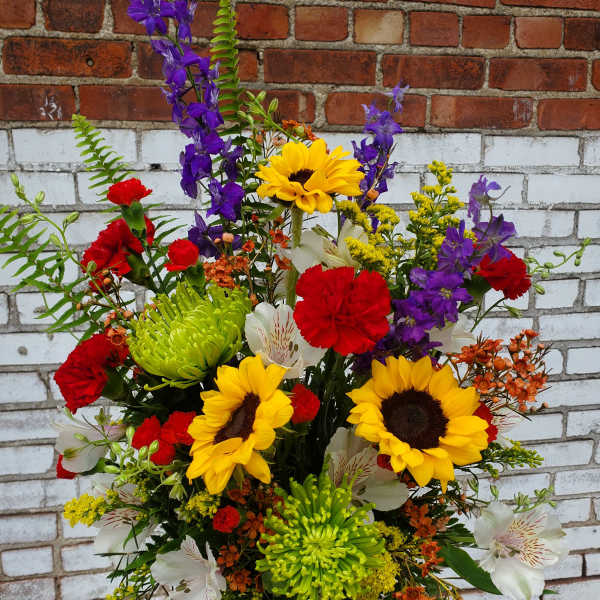 Mixed bouquet with sunflowers, red carnations, and purple blooms in a patterned vase