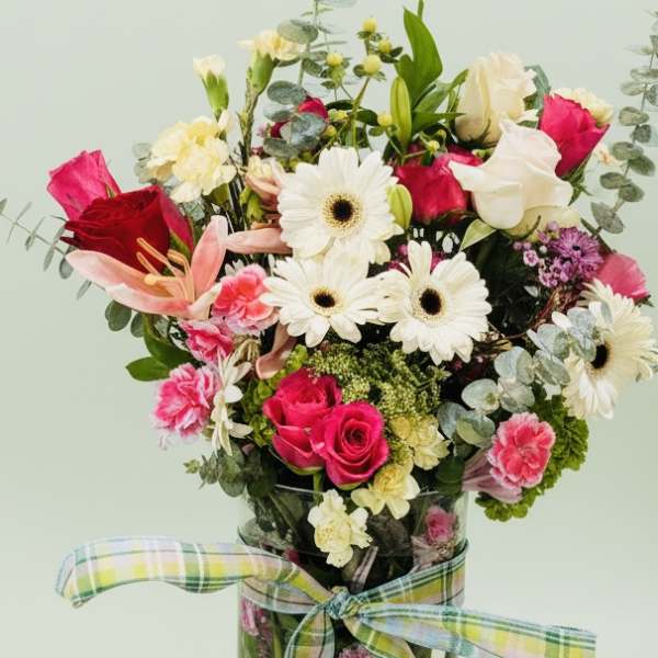 Mixed bouquet of pink and white flowers in a glass vase with a plaid ribbon