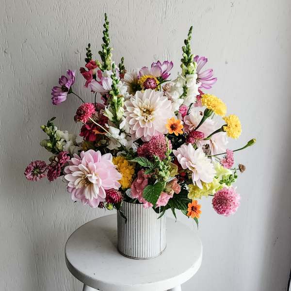 Mixed bouquet of pink, white, yellow, and purple flowers in a ribbed white vase