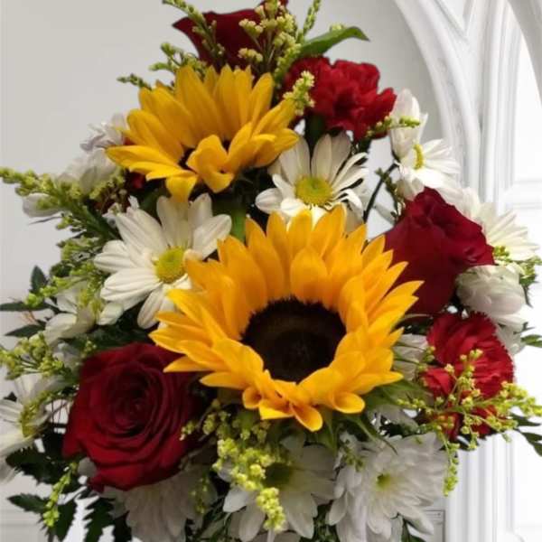 Bouquet of sunflowers, red roses, and white daisies in a rustic vase