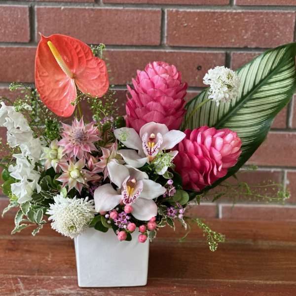 Tropical floral arrangement in a white square vase with pink and white blooms