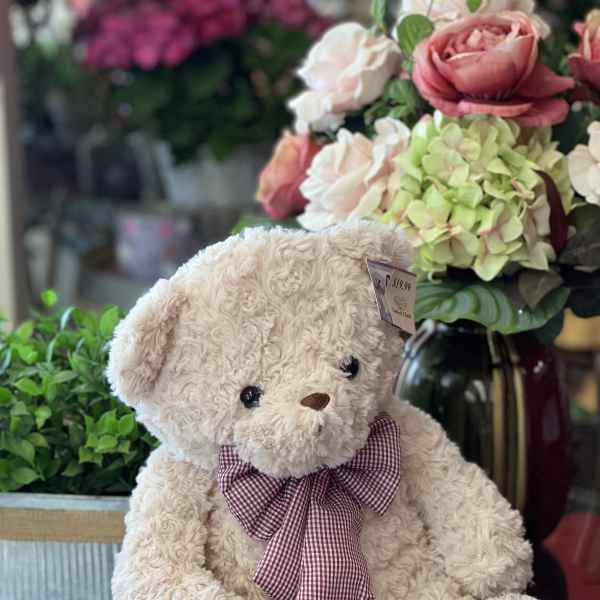 Plush teddy bear with a plaid bow sitting beside a floral arrangement