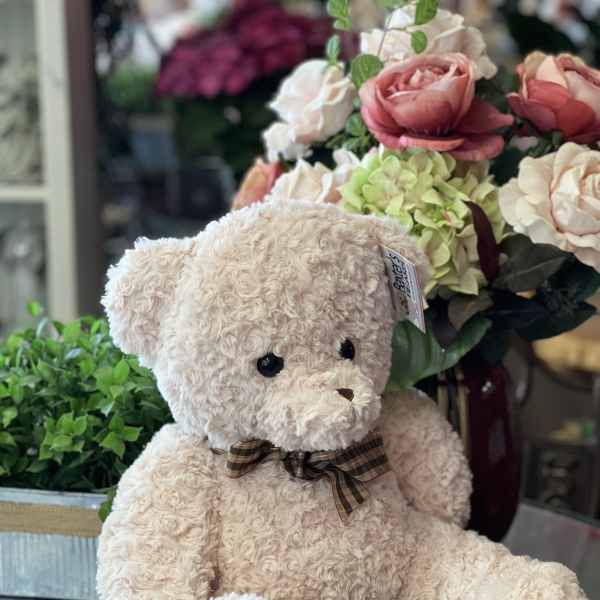 Teddy bear in front of a floral arrangement with pink and cream roses