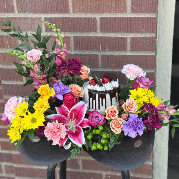 Colorful floral arrangement with a small cake centerpiece in a black container
