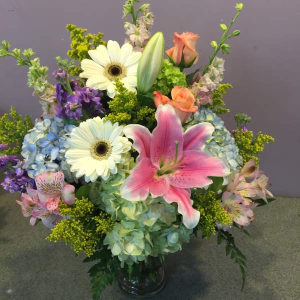 Mixed bouquet with pink lily, white daisies, and blue hydrangeas in a glass vase