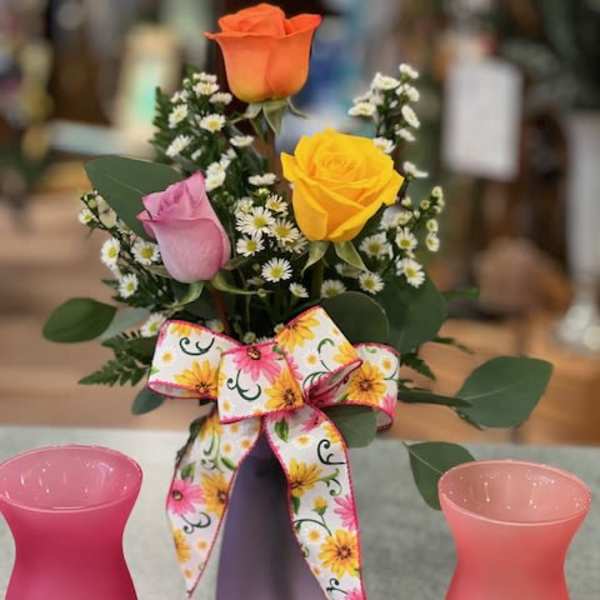 Small bouquet of roses and white filler flowers in a purple vase with a floral bow.
