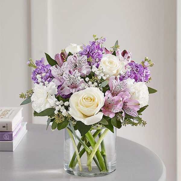 Bouquet of white roses and purple flowers in a clear glass vase