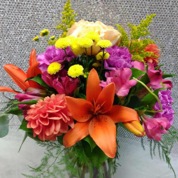 Colorful bouquet with orange lilies, pink flowers, and yellow blooms in a glass vase