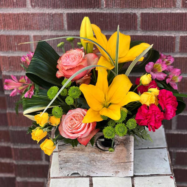 Colorful bouquet with yellow lilies, pink roses, and bright pink carnations in a wooden box