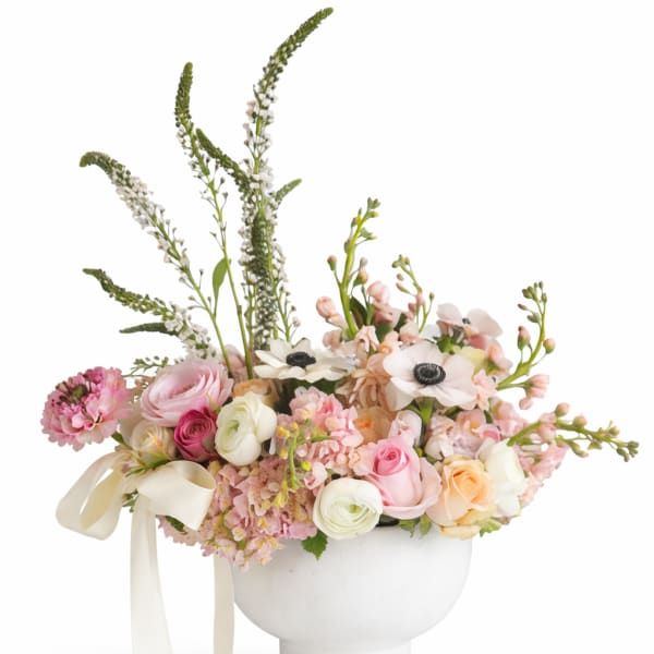 Pastel floral arrangement in a white pedestal vase with ribbon