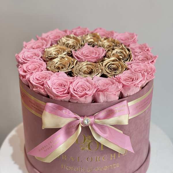 Pink and gold roses arranged in a round hat box with a ribbon bow