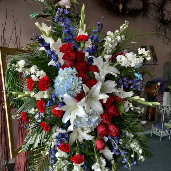 Large standing floral spray with red roses, white lilies, and blue flowers
