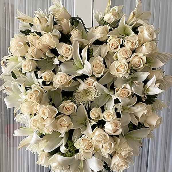 Heart-shaped standing spray of ivory roses and white lilies on a metal easel