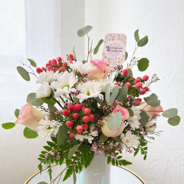 Bouquet of white daisies, pink roses, and red berries in a glass vase