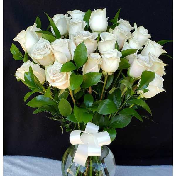 White roses arranged in a glass vase with a white ribbon