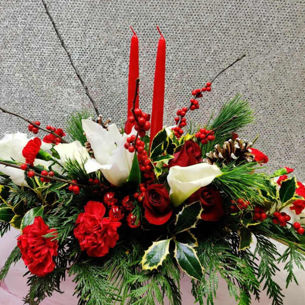 Holiday arrangement with red and white flowers, candles, and pinecones