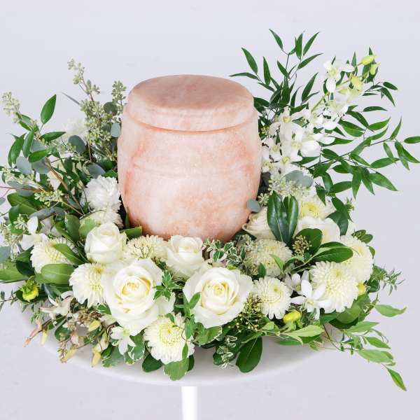 White roses and mums arranged around a pink urn-shaped vessel