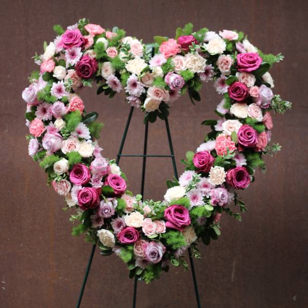 Heart-shaped floral wreath on a stand with pink and white roses