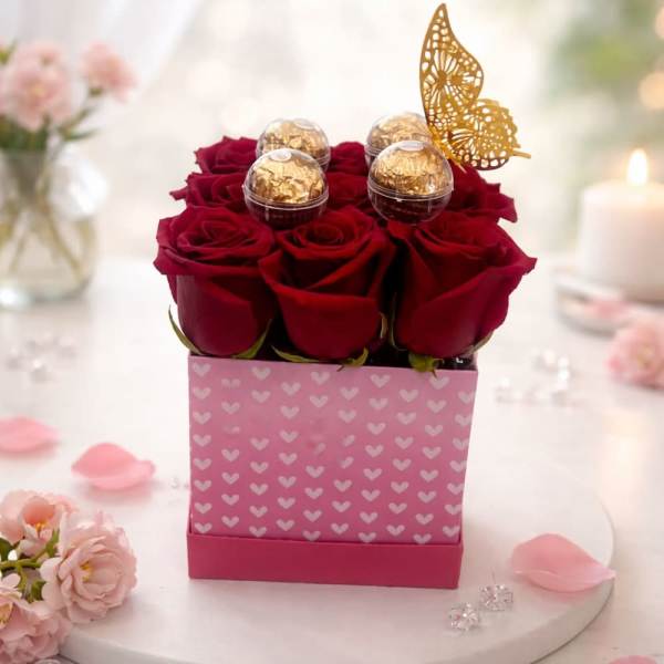 Red roses in a pink heart-patterned box with gold chocolates and a butterfly topper