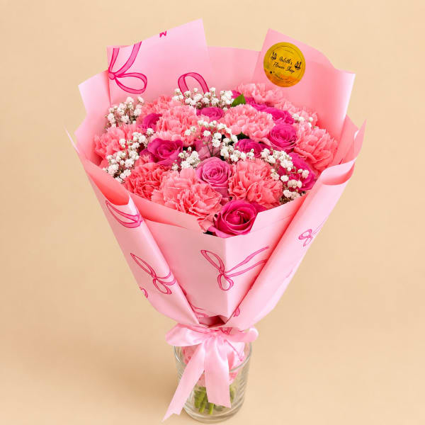 Pink bouquet of carnations and roses wrapped in pink paper in a glass vase