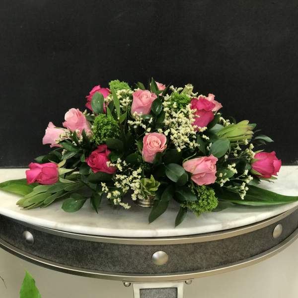 Low arrangement of light and hot pink roses with white filler flowers in a silver container