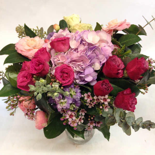Mixed pink, purple, and red roses in a clear glass vase